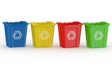 Immagine con quattro contenitori per la raccolta differenziata allineati su sfondo chiaro. I bidoni sono di colore blu, giallo, rosso e verde e riportano sul lato frontale il simbolo bianco del riciclo.